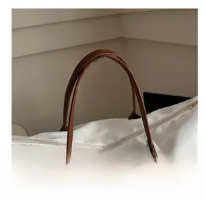 Close-up of durable brown leather handles and stitching on a large white nylon tote bag