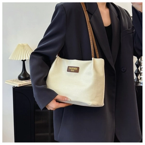 Detail of waffle-weave shoulder tote bag with brown leather straps and branded logo tag