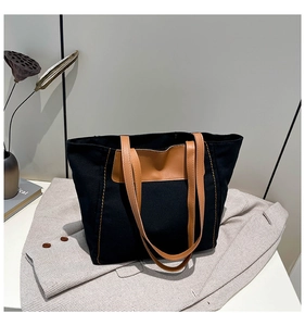 Detail of black canvas tote bag with brown leather handles and contrast stitching