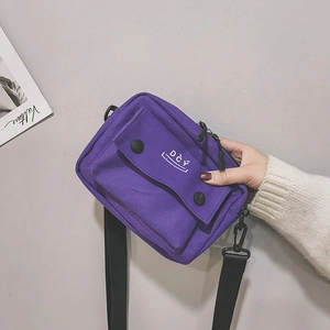 Detail of purple canvas crossbody bag showing DCY smiley logo and black strap clips