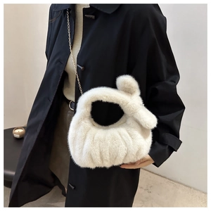 Détail d'un sac en peluche blanc avec chaîne dorée porté sur une tenue élégante
