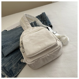 Detail of off-white multi-zipper casual bag with silver hardware on a textured surface