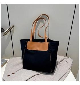 Detail of black canvas tote bag showing brown leather handles and contrast stitching