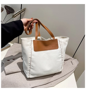 Detail of canvas tote bag showing contrast brown leather straps and premium stitching