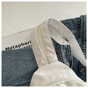 Close-up of white textured sling bag featuring a wide nylon strap and zipper detail