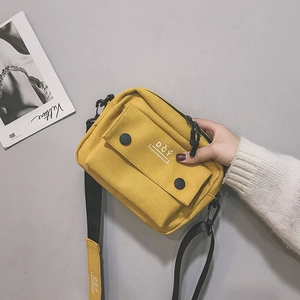 Close-up of yellow canvas shoulder bag featuring DCY logo and black buckled front pocket