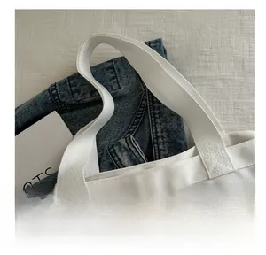 Detail showing the sturdy white canvas tote bag handle and stitching against a blue denim jacket