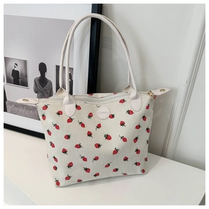 Detailed texture of white corduroy tote bag featuring red strawberry prints and leather handles