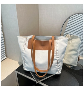Detail of canvas tote bag showing brown faux leather handles and contrast stitching