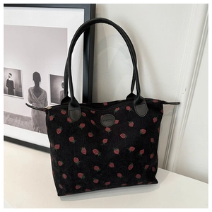 Detail of strawberry embroidery on black corduroy tote bag with leather straps and logo