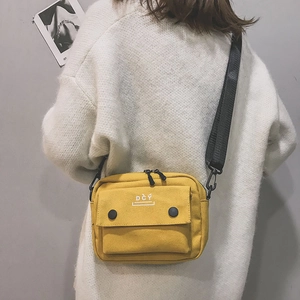 Detail of yellow canvas crossbody bag featuring functional front pockets and wide black strap