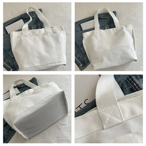Detail view of white canvas tote bag with triple front pockets and reinforced cross stitching