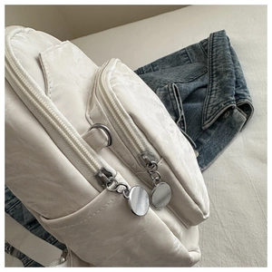 Detail of white nylon backpack featuring silver round zipper pulls and textured fabric