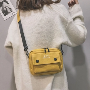 Detail view of yellow canvas crossbody bag featuring functional pockets and black straps