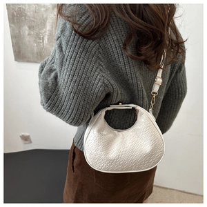 Détail du sac demi-lune blanc texturé porté avec bandoulière réglable et boucles dorées