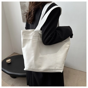 Detail of a large white canvas tote bag with wide shoulder straps shown on a model