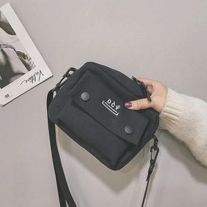 Detail of a black canvas crossbody bag featuring DCY logo and snap-button flap pocket
