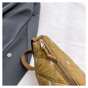 Detail der khakifarbenen Stepptasche mit weißer Schleifenstickerei und Metallreißverschluss