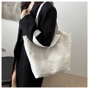 Detail showing the thick canvas texture and functional side pocket of the white tote bag