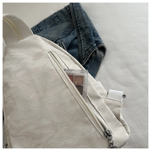 Close-up of white wrinkled nylon crossbody bag with zipper pocket and denim jacket decor