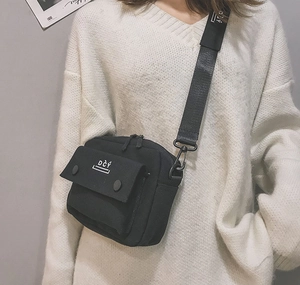 Model wearing a black canvas crossbody bag with DĊÝ logo and wide adjustable strap