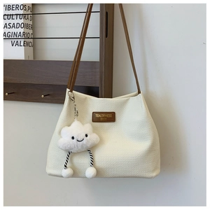 Detail of waffle textured cream tote bag with brown straps and white cloud pendant charm