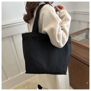 Detail of a large black canvas tote bag with a front pocket shown on a model side view