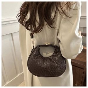 Détail de la texture tressée d'un sac demi-lune marron foncé porté à l'épaule