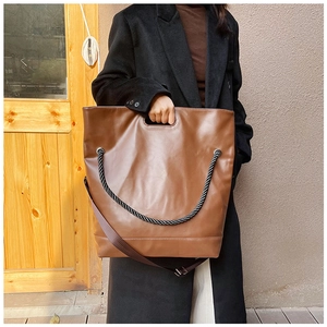 Detail of a large brown tote bag with black rope handles and adjustable shoulder strap