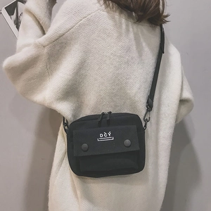 Detail view of black canvas crossbody bag with white logo and double buckle front pocket