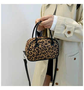 Detailed view of leopard print handbag with black leather handles and shoulder strap