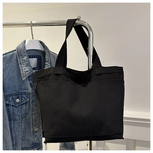 Detail view of black canvas tote bag showing wide front pocket and durable carry straps