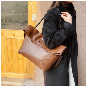 Detail of a brown soft leather tote bag featuring a black braided rope strap and fold closure