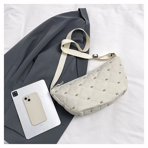 Detail der beigefarbenen Stepptasche mit feiner Schleifenstickerei und verstellbarem Gurt
