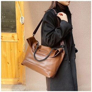 Detail of a brown leather tote bag with black woven handles and a detachable shoulder strap