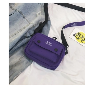Detail of a purple canvas crossbody bag with front pocket and DCY logo on a white cloth
