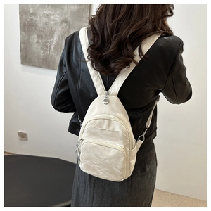Detail view of cream white textured leather backpack showing the multi-layer zippers on a model