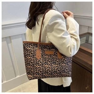 Leopard print tote bag with brown straps shown on shoulder in a minimalist indoor setting