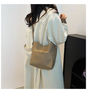 Detailed view of khaki lychee leather bucket bag worn by model in white trench coat