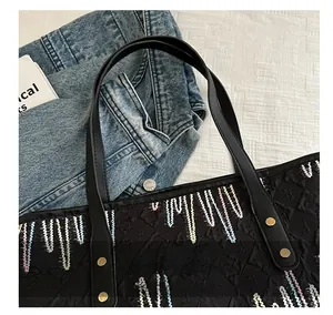 Détail du sac cabas noir montrant les coutures zigzag colorées et la poignée en cuir