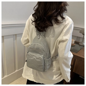 Detail view of silver textured mini backpack on model's back in a modern room