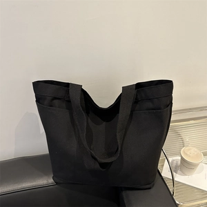 Minimalist large capacity black canvas tote bag on a leather sofa in a modern setting