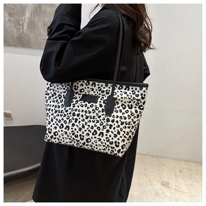 Detailed view of leopard print tote bag with black shoulder straps and leather patch