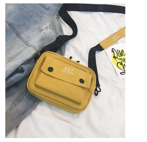 Detail of yellow canvas crossbody bag with black adjustable strap and brand logo