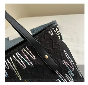 Détail de couture d'un sac cabas noir avec broderie ondulée colorée et rivets dorés en métal