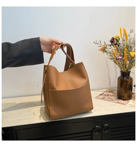 Detail view of large brown lychee pattern leather tote bag on wooden counter with dry flowers