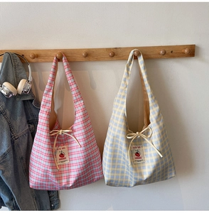 Detail of plaid canvas tote bag showing handmade label and cherry pattern on a wooden hook