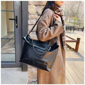 Detail of black faux leather tote bag with unique woven rope handles in an outdoor setting