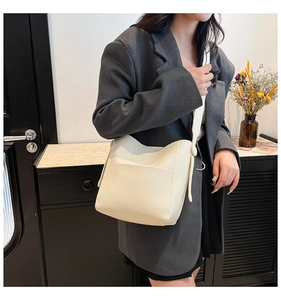 Detailed side view of a cream-colored pebbled leather bucket bag worn by a model