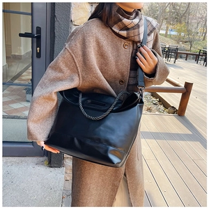 Detail of a black leather tote bag with braided handles and an adjustable shoulder strap